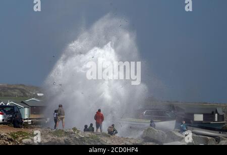 Les gens se tiennent à côté d'un trou de soufflage alors que les vagues s'écrasent contre le rivage à Portland Bill à Dorset. Banque D'Images