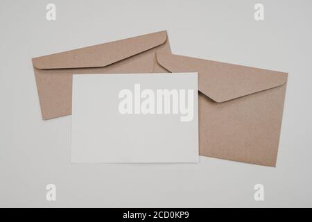 Papier blanc vierge sur les deux enveloppes de papier marron. Maquette de carte de vœux vierge horizontale. Vue de dessus de l'enveloppe de papier artisanal sur fond blanc. FL Banque D'Images