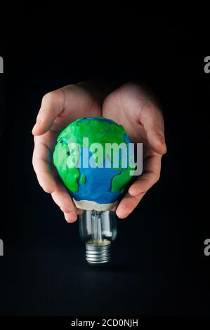 Concept de l'heure de la Terre: Mains mâles tenant une lampe électrique décorée comme plaline modèle de planète Terre sur fond noir avec espace vide pour le texte Banque D'Images