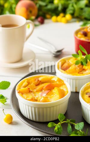 Délicieux clafoutis à base de yaourt blanc et de pêches, de prune de cerise et de dessert de pêche dans des bols en forme de porc sur la table avec une tasse de jus Banque D'Images