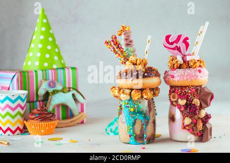 Concept de fête d'enfants : deux garnitures de freak milk-shakes avec beignet, pop-corn au caramel et bonbons sur la table de fête d'anniversaire d'enfants ; mise au point sélective Banque D'Images
