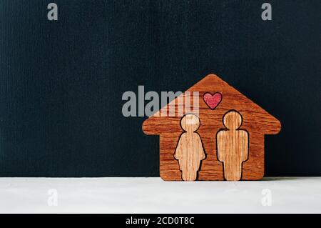 Concept de maison familiale. Maison en bois avec des figures d'homme et de femme à l'intérieur sur fond noir tableau de craie avec espace vide pour le texte. Banque D'Images