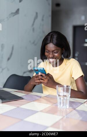 Une femme africaine debout dans la cuisine a reçu sms lire le message utilise le téléphone. Banque D'Images