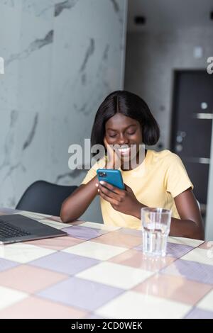 Une femme africaine debout dans la cuisine a reçu sms lire le message utilise le téléphone. Banque D'Images