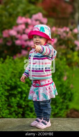 Portrait d'une jeune fille debout dans le parc portant une tenue colorée et montrant quelque chose; Surrey, Colombie-Britannique, Canada Banque D'Images