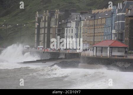 Aberystwyth pays de Galles Royaume-Uni météo 25 août 2020 : de fortes pluies et des vents violents battent les régions côtières du pays de Galles, de forts vents déferlent dans d'énormes vagues qui se brisent contre les défenses maritimes d'Aberystwyth. Les vacanciers bravent la force gale pendant une promenade de l'après-midi de tempête le long de la promenade, crédit: mike davies/Alamy Live News Banque D'Images