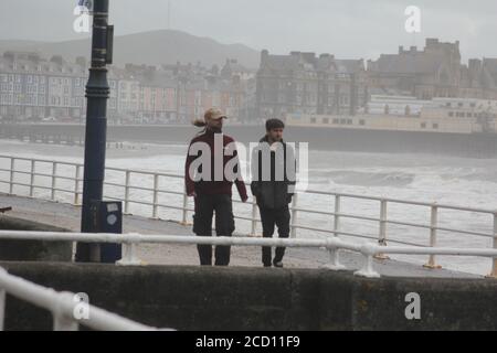 Aberystwyth pays de Galles Royaume-Uni météo 25 août 2020 : de fortes pluies et des vents violents battent les régions côtières du pays de Galles, de forts vents déferlent dans d'énormes vagues qui se brisent contre les défenses maritimes d'Aberystwyth. Les vacanciers bravent la force gale pendant une promenade de l'après-midi de tempête le long de la promenade, crédit: mike davies/Alamy Live News Banque D'Images