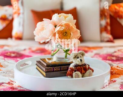 Bouquet de pivoines de couleur pêche, livres et petit ours en laine un plateau de lit sur un lit à fleurs literie à motifs Banque D'Images