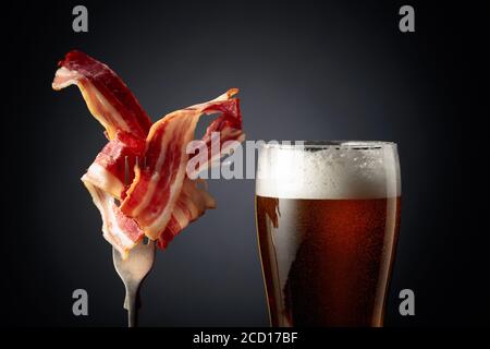 Bière et tranches de bacon sur fond noir. Banque D'Images