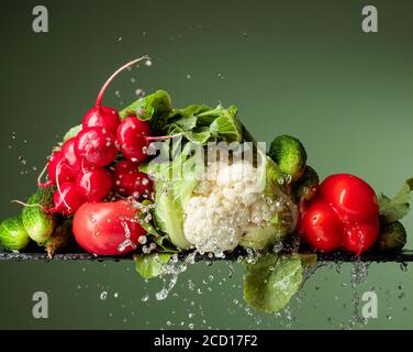 Légumes crus dans les éclaboussures d'eau. Chou-fleur, tomate, concombre, radis et paprika sur fond vert. Banque D'Images