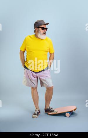 Homme patineur. Portrait de l'homme hipster senior en lunettes isolées sur fond bleu clair de studio. Concept de mode de vie technologique et joyeux pour les personnes âgées. Couleurs tendance, toujours jeune. CopySpace pour votre annonce. Banque D'Images