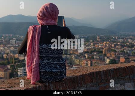 Fille égyptienne avec smartphon sur le toit-terrasse avec vue aérienne de la vieille ville italienne Brescia. Banque D'Images