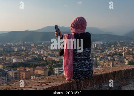 Fille égyptienne avec smartphon sur le toit-terrasse avec vue aérienne de la vieille ville italienne Brescia. Banque D'Images