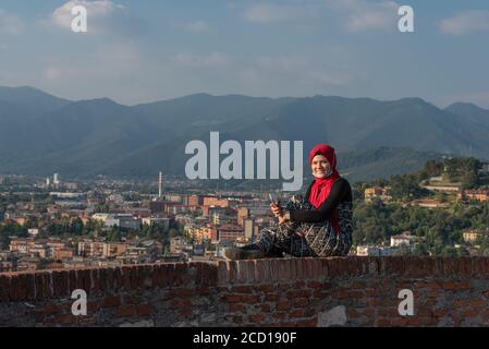 Fille égyptienne avec smartphon sur le toit-terrasse avec vue aérienne de la vieille ville italienne Brescia. Banque D'Images