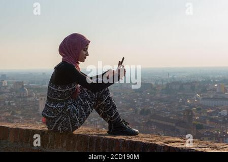 Fille égyptienne avec smartphon sur le toit-terrasse avec vue aérienne de la vieille ville italienne Brescia. Banque D'Images