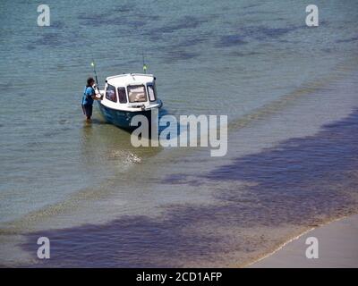 Homme tenant un petit bateau de croisière en cabine dans les eaux peu profondes de la plage de Porthcurnick, Cornwall, Royaume-Uni Banque D'Images
