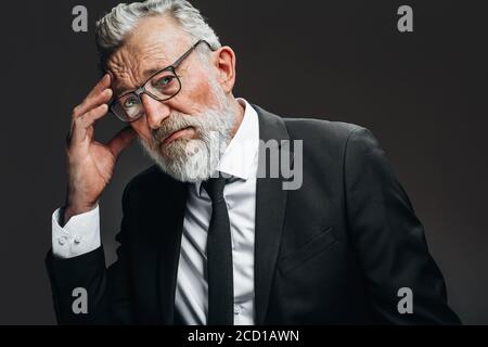 Homme d'affaires senior dans ses années 70 avec des cheveux gris et la barbe ayant des maux de tête et des temples frottant, regardant la caméra avec les yeux fatigués de douleur, isolés plus Banque D'Images