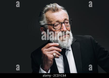 Homme politique mature et confiant, vêtu d'un costume habillé noir avec cravate au cou pendant le processus de travail, en regardant attentif, isolé sur fond sombre Banque D'Images