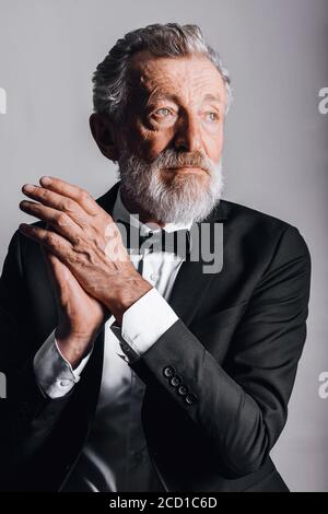 Homme âgé officiel habillé de smoking noir avec noeud papillon regarder la caméra avec une expression sûre et sérieuse Banque D'Images