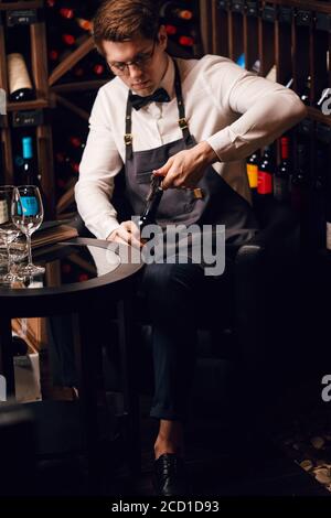 Jeune sommelier élégant tirant le liège d'une bouteille à l'aide d'un couteau de sommelier. Photo rognée d'une bouteille de vin rouge ouvrante avec bouchon à vis au repos Banque D'Images