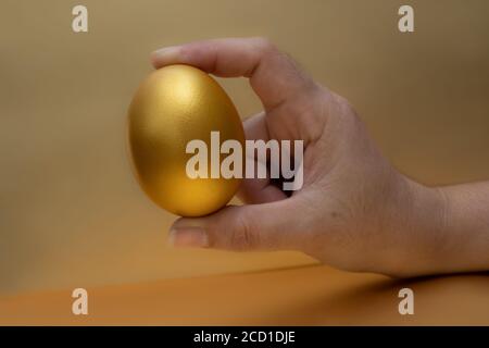 Femme main tenant l'oeuf d'or sur le fond doré Banque D'Images