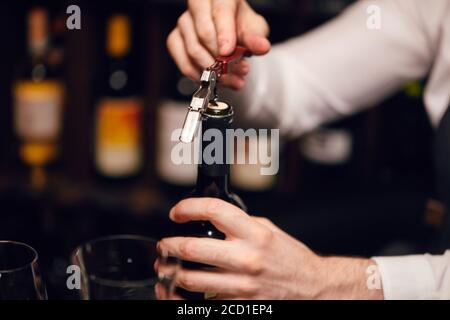 Retirer le liège d'une bouteille à l'aide d'un couteau de sommelier, en gros plan. Photo rognée d'une bouteille de vin rouge ouverte par le serveur. Banque D'Images