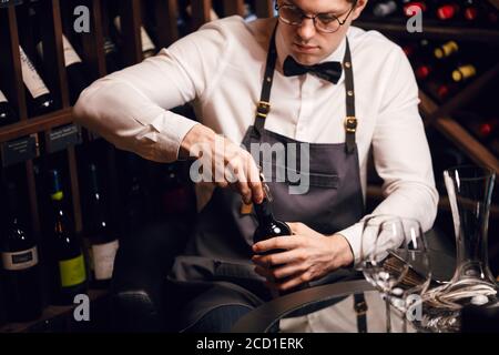 Jeune sommelier élégant tirant le liège d'une bouteille à l'aide d'un couteau de sommelier. Photo rognée d'une bouteille de vin rouge ouvrante avec bouchon à vis au repos Banque D'Images