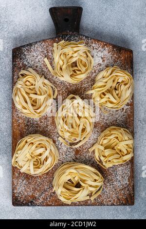 Tagliatelle. Pâtes italiennes traditionnelles non cuites faites maison sur un panneau en bois sur fond de béton gris. Mise au point sélective Banque D'Images