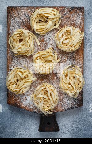 Tagliatelle. Pâtes italiennes traditionnelles non cuites faites maison sur un panneau en bois sur fond de béton gris. Mise au point sélective Banque D'Images