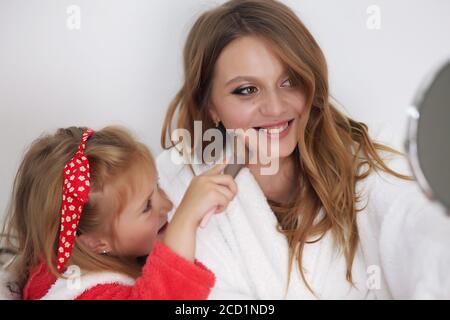 Photo de mère et de fille en manteaux blancs. Ils sont assis sur le canapé Banque D'Images