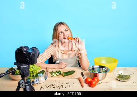 Photo isolée d'une diététiste féminine qui se met à la carotte fraîche pendant la pause entre deux prises de vue vidéo pour son blog sur les aliments sains, en regardant de côté avec dre Banque D'Images