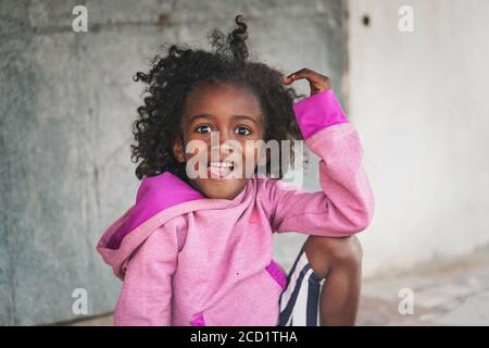 Ranohira, Madagascar - 29 avril 2019: Petite fille en sweat-shirt rose souriant dans la caméra avec sa langue notre. Les gens de Madagascar, en particulier les Malagas Banque D'Images