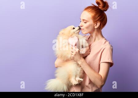 drôle adorable chien embrassant propriétaire pendant qu'elle le tient. portrait de gros plan, isolé bleu fond, Banque D'Images