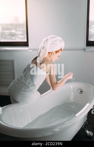 Routine matinale de beauté rouge dans la salle de bains. Femme courant bain, veut se rafraîchir dans l'eau. Banque D'Images