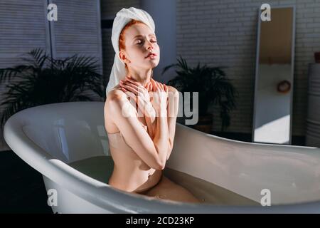 Belle jeune femme se dorloter dans l'eau, prendre un bain avec des huiles minérales dans l'atmosphère relaxante de la zone spa de l'hôtel au matin ensoleillé Banque D'Images