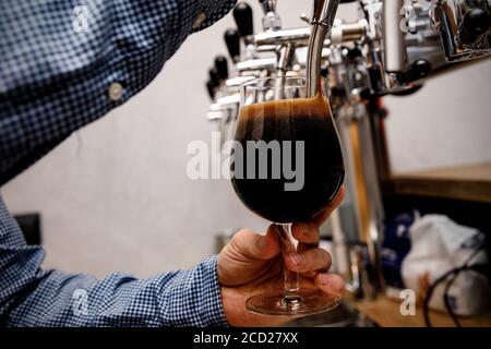 Le barman verse de la bière fraîche et foncée du robinet au pub. Banque D'Images