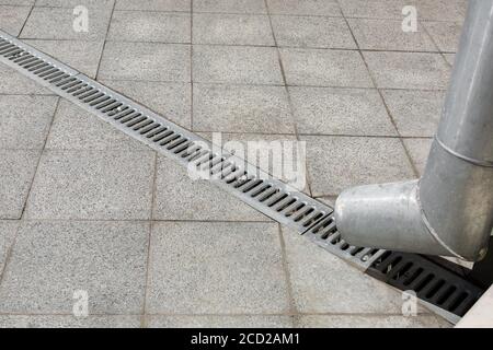 une structure d'ingénierie un bec verseur avec une grille de drainage pour drainage de l'eau de pluie sur un fond de pierre grise trottoir en granit de la place Banque D'Images