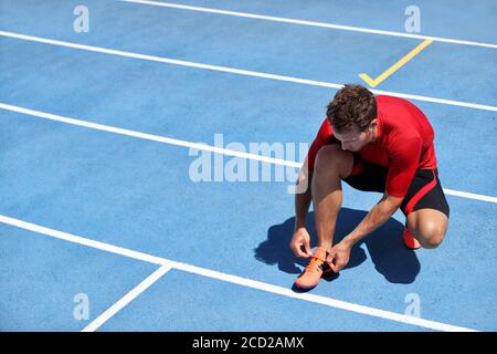 Athlète sprinter se prépare à courir attacher les lacets de chaussures sur les pistes de course du stade. Homme coureur se préparant pour l'entraînement marathon de course en plein air. Fitness Banque D'Images