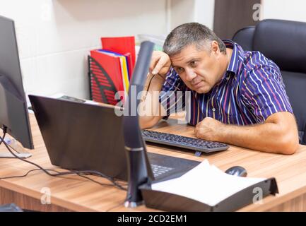 Triste homme d'âge moyen devant un ordinateur portable au bureau. Travail en ligne. Banque D'Images