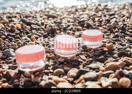 Bocaux pour crème avec couvercles roses sur galet brun. Brillance du soleil. Banque D'Images