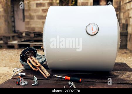 chaudière démontée, située à côté de l'élément chauffant, écrous et outils sur une surface en bois, à l'extérieur. Banque D'Images