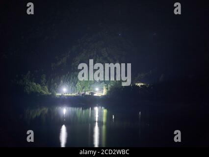 Lac de barrage et installation industrielle dans les montagnes la nuit avec des lumières réfléchissantes sur l'eau Banque D'Images