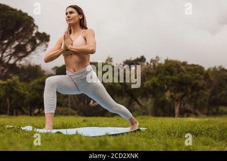 femme de fitness pratiquant le yoga dans un parc. Portrait d'une femme faisant des fentes en avant tout en pratiquant le yoga à l'extérieur. Banque D'Images