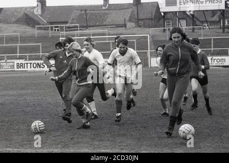 Années 1980, histoire, deux filles en costume de sport qui ont un coup d'envoi sur le terrain de football du York City FC sont pourchassés par des garçons, tous les jeunes qui travaillent sur le terrain ayant un peu de plaisir avant le match. Les terrasses de football de salon étaient les spectateurs debout et regarder un match peut être vu. Banque D'Images