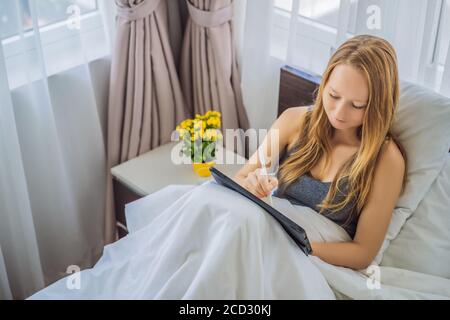 Femme tire sur une tablette avec un stylet dans le lit Banque D'Images