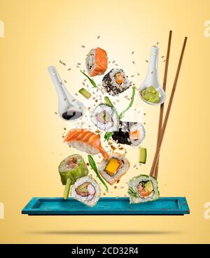 Des sushis volants sont servis sur une assiette, séparés sur un fond coloré. De nombreuses sortes de sushis populaires avec des baguettes. Concept de plat asiatique volant W Banque D'Images
