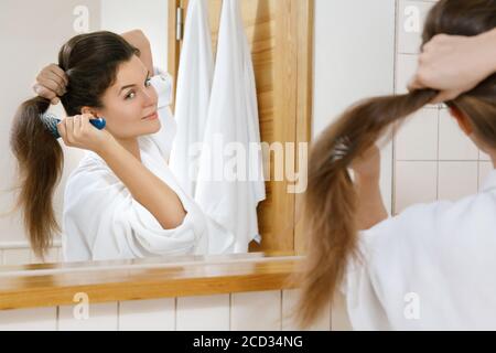 Jeune femme avec un beau cheveux fort regardant dans le miroir Banque D'Images