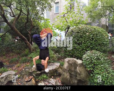 M. Jiang, un homme dans ses années soixante-dix, pratique le yoga d'une manière spéciale, debout à l'envers avec sa tête tout en tenant un parapluie avec son pied sur un ro Banque D'Images