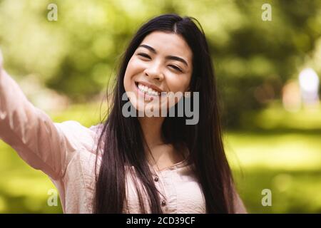 Le plaisir du selfie. Belle fille asiatique souriante prenant un autoportrait en plein air, en prenant des photos Banque D'Images