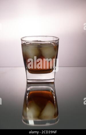 Verre de whisky avec morceaux de glace sur la table miroir. Image verticale avec espace de copie. Banque D'Images